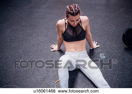 Stock Photo - Young woman training, sitting on gym floor taking a break. Fotosearch