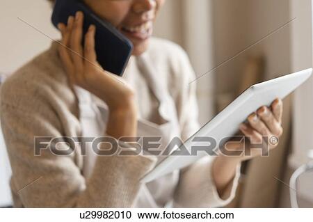 Stock Image - Young woman using digital tablet while taking phone call. Fotosearch