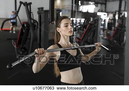 Stock Image - Young woman using exercise machine in gym. Fotosearch