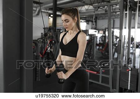 Stock Image - Young woman using exercise machine in gym. Fotosearch