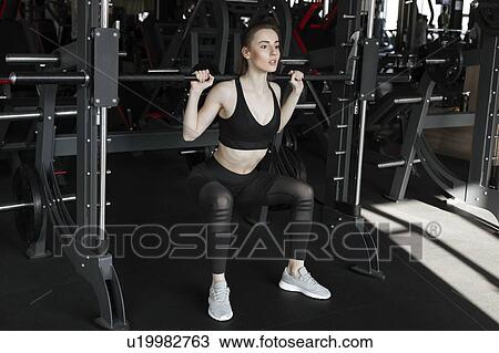 Stock Image - Young woman using exercise machine in gym. Fotosearch