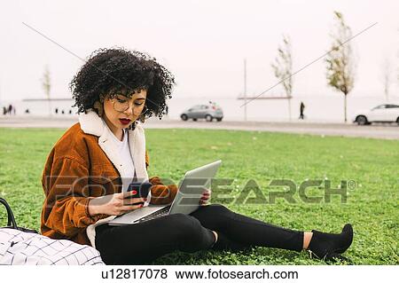 Young woman using laptop and smart phone in park View Large Photo Image Stock Photo - Young woman using laptop and smart phone in park. Fotosearch