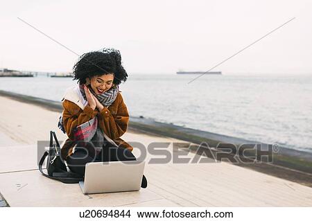Picture - Young woman using laptop on waterfront in Lisbon, Portugal. Fotosearch