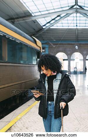 Stock Photograph - Young woman using smart phone in railway station. Fotosearch