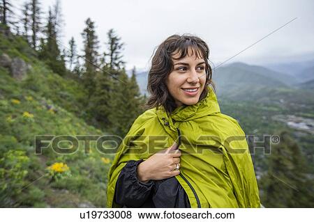 Stock Photo - Young woman wearing green raincoat on hike. Fotosearch