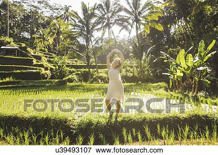 Stock Photo - Young woman wearing white dress in rice paddy in Bali, Indonesia. Fotosearch