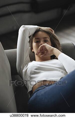 Stock Photo - Young woman wearing white sweater lying on sofa. Fotosearch