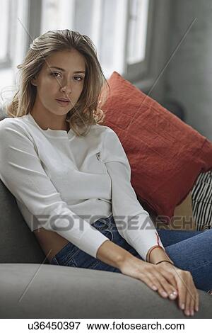Stock Photo - Young woman wearing white sweater on sofa. Fotosearch