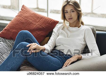 Stock Photo - Young woman wearing white sweater on sofa. Fotosearch