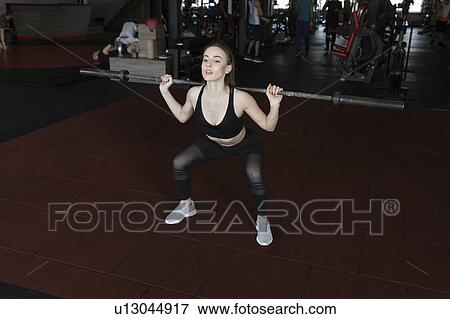 Stock Photo - Young woman weight lifting in gym. Fotosearch