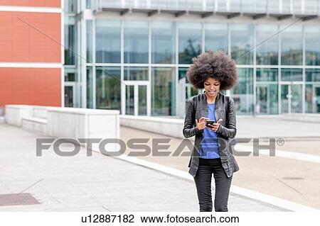 Young woman with afro hair in city, using smartphone touchscreen View Large Photo Image Stock Image - Young woman with afro hair in city, using smartphone touchscreen. Fotosearch