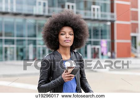 Young woman with afro hair in city, holding smartphone and takeaway coffee, portrait View Large Photo Image Stock Photo - Young woman with afro hair in city, holding smartphone and takeaway coffee, portrait. Fotosearch