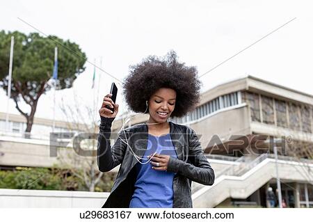 Young woman with afro hair in city, walking and listening to smartphone music View Large Photo Image Stock Photo - Young woman with afro hair in city, walking and listening to smartphone music. Fotosearch