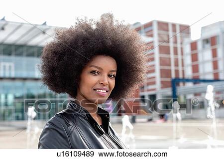 Stock Photo - Young woman with afro hair on city concourse, portrait. Fotosearch