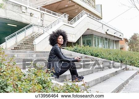 Young woman with afro hair sitting on city stairway looking away View Large Photo Image Picture - Young woman with afro hair sitting on city stairway looking away. Fotosearch