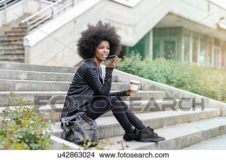 Young woman with afro hair sitting on city stairway, talking to smartphone View Large Photo Image Picture - Young woman with afro hair sitting on city stairway, talking to smartphone. Fotosearch