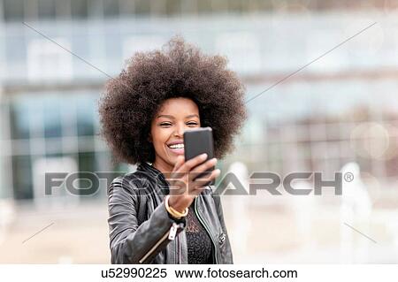 Young woman with afro hair taking smartphone selfie on city concourse View Large Photo Image Stock Photography - Young woman with afro hair taking smartphone selfie on city concourse. Fotosearch