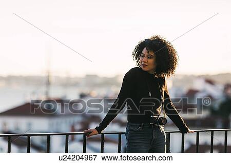 Stock Photo - Young woman with camera leaning on railing. Fotosearch