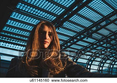 Stock Image - Young woman with long blond hair in train station, low angle portrait, Turin, Piemonte, Italy. Fotosearch