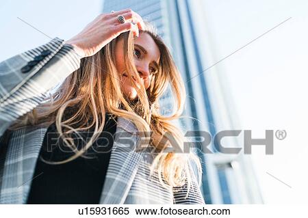 Stock Photography - Young woman with long blond hair in front of skyscraper, low angle view, Turin, Piemonte, Italy. Fotosearch