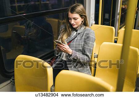 Picture - Young woman with long blond hair on carriage looking at smartphone at night. Fotosearch
