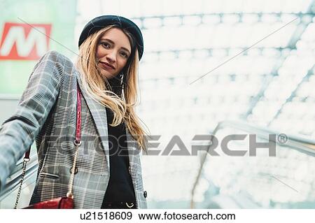Stock Photo - Young woman with long blond hair on train station escalator, low angle portrait, Turin, Piemonte, Italy. Fotosearch