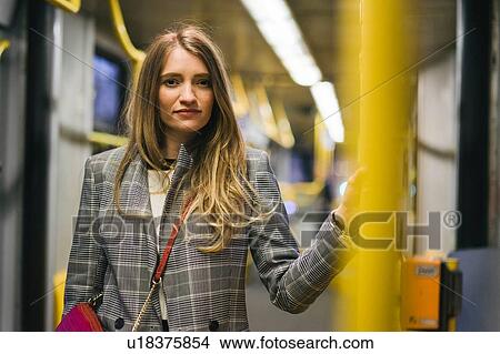 Picture - Young woman with long blond hair standing in train carriage, portrait. Fotosearch