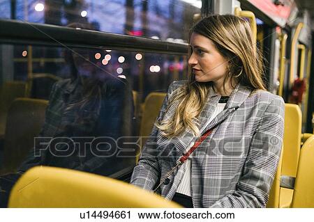 Stock Image - Young woman with long blond hair looking out through train carriage window at dusk. Fotosearch