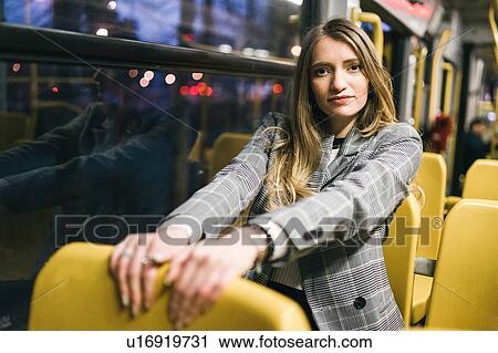 Stock Image - Young woman with long blond hair sitting in train carriage at dusk, portrait. Fotosearch