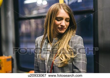 Stock Photo - Young woman with long blond hair looking down in train carriage at dusk. Fotosearch