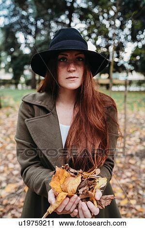 Young woman with long red hair holding autumn leaves in park, portrait View Large Photo Image Stock Image - Young woman with long red hair holding autumn leaves in park, portrait. Fotosearch