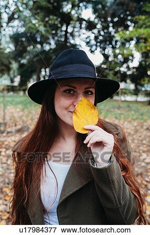 Young woman with long red hair holding autumn leaf on nose in park, portrait View Large Photo Image Stock Photo - Young woman with long red hair holding autumn leaf on nose in park, portrait. Fotosearch