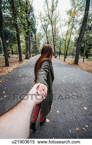 Stock Photography - Young woman with long red hair holding boyfriend's hand in autumn park, personal perspective. Fotosearch