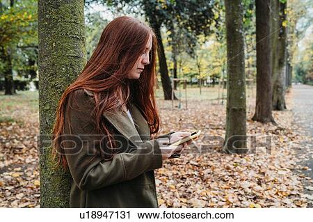 Young woman with long red hair in autumn park looking at smartphone View Large Photo Image Stock Image - Young woman with long red hair in autumn park looking at smartphone. Fotosearch