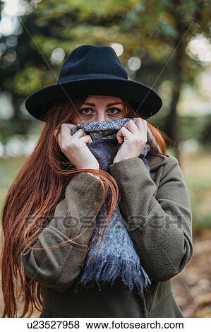 Stock Photo - Young woman with long red hair in autumn park covering mouth with scarf, portrait. Fotosearch