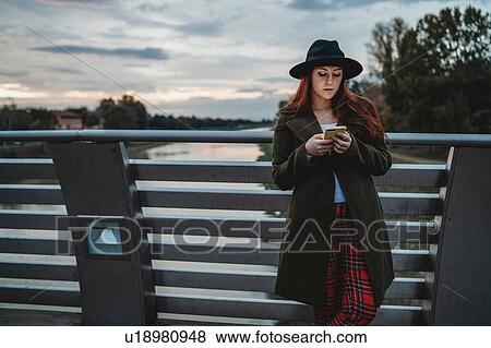 Young woman with long red hair leaning on footbridge looking at smartphone at dusk, Florence, Tuscany, Italy View Large Photo Image Stock Photo - Young woman with long red hair leaning on footbridge looking at smartphone at dusk, Florence, Tuscany, Italy. Fotosearch