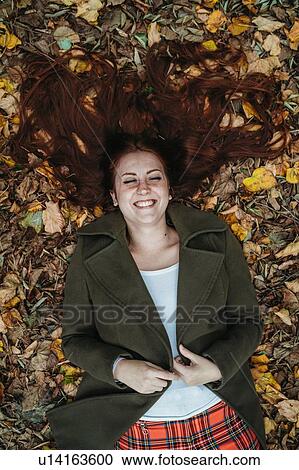 Young woman with long red hair lying amongst autumn leaves laughing, overhead view View Large Photo Image Stock Image - Young woman with long red hair lying amongst autumn leaves laughing, overhead view. Fotosearch