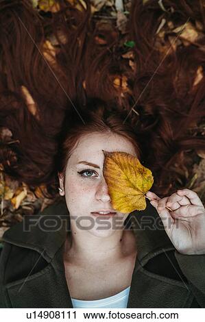 Young woman with long red hair lying amongst autumn leaves and covering eye with autumn leaf, overhead portrait View Large Photo Image Stock Image - Young woman with long red hair lying amongst autumn leaves and covering eye with autumn leaf, overhead portrait. Fotosearch