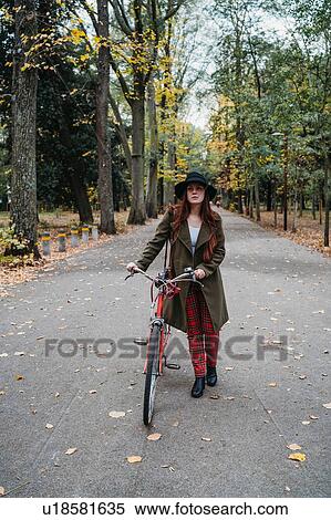 Young woman with long red hair pushing bicycle in tree lined autumn park, portrait, Florence, Tuscany, Italy View Large Photo Image Stock Photography - Young woman with long red hair pushing bicycle in tree lined autumn park, portrait, Florence, Tuscany, Italy. Fotosearch