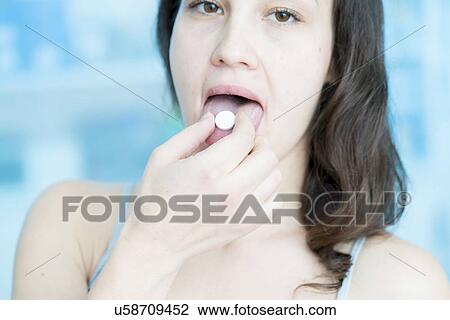 Stock Image - Young woman with pill on tongue.. Fotosearch
