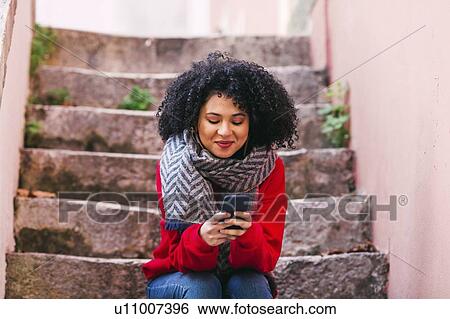 Stock Photograph - Young woman with smart phone sitting on steps. Fotosearch