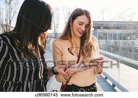 Young women outside office building looking at smartphone, Turin, Piemonte, Italy View Large Photo Image Stock Photography - Young women outside office building looking at smartphone, Turin, Piemonte, Italy. Fotosearch