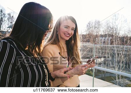 Young women outside sunlit office building looking at smartphone, Turin, Piemonte, Italy View Large Photo Image Stock Photo - Young women outside sunlit office building looking at smartphone, Turin, Piemonte, Italy. Fotosearch