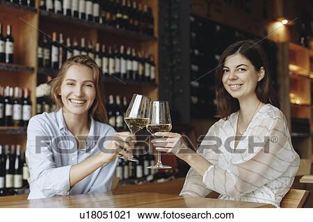 Stock Image - Young women toasting with glasses of white wine. Fotosearch