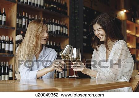 Stock Image - Young women toasting with glasses of white wine. Fotosearch