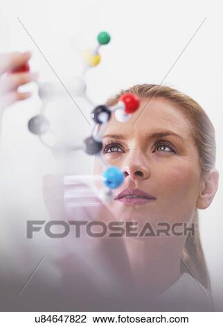 Stock Image - Chemistry research, conceptual image. Scientist using a molecular model to understand a chemical formula.. Fotosearch