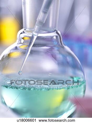 Stock Image - Chemistry research. Scientist taking a sample from a laboratory flask containing a chemical formula with a pipette.. Fotosearch