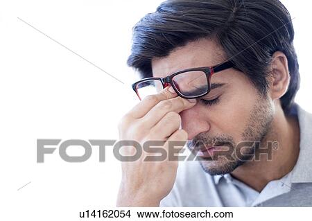 Picture - Man pinching the bridge of his nose, wearing glasses.. Fotosearch