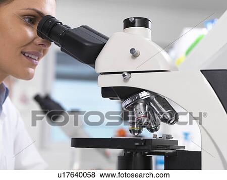 Stock Photo - Medical screening. Scientist examining a glass slide containing a human sample under a microscope.. Fotosearch