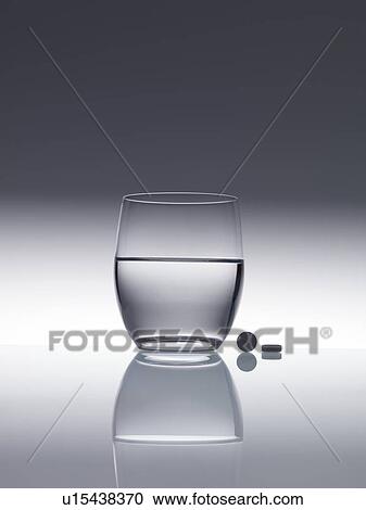 Tablets next to a glass of water. View Large Photo Image Stock Image - Tablets next to a glass of water.. Fotosearch